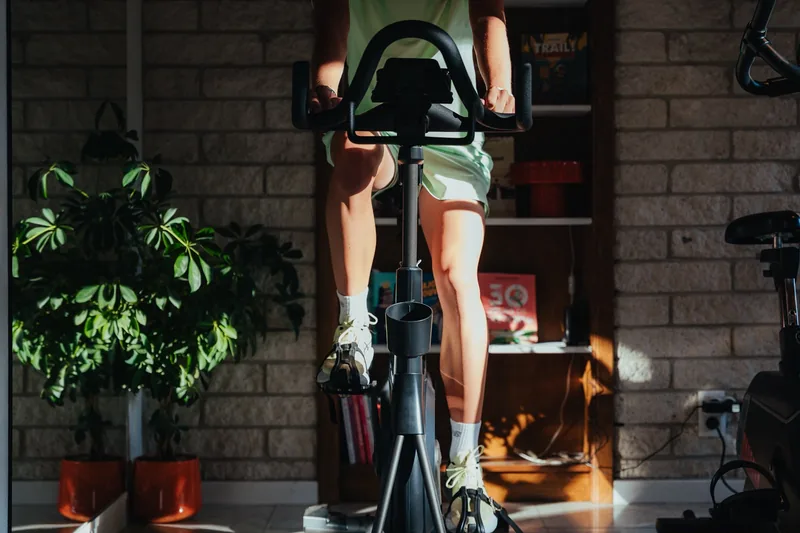 Jambes d'un cycliste en train de pédaler sur un vélo d'intérieur, plantes vertes en arrière-plan.