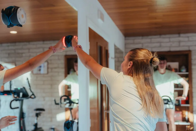 Personne en salle de sport tendant le bras vers un dispositif lumineux suspendu, vélos d'intérieur en fond