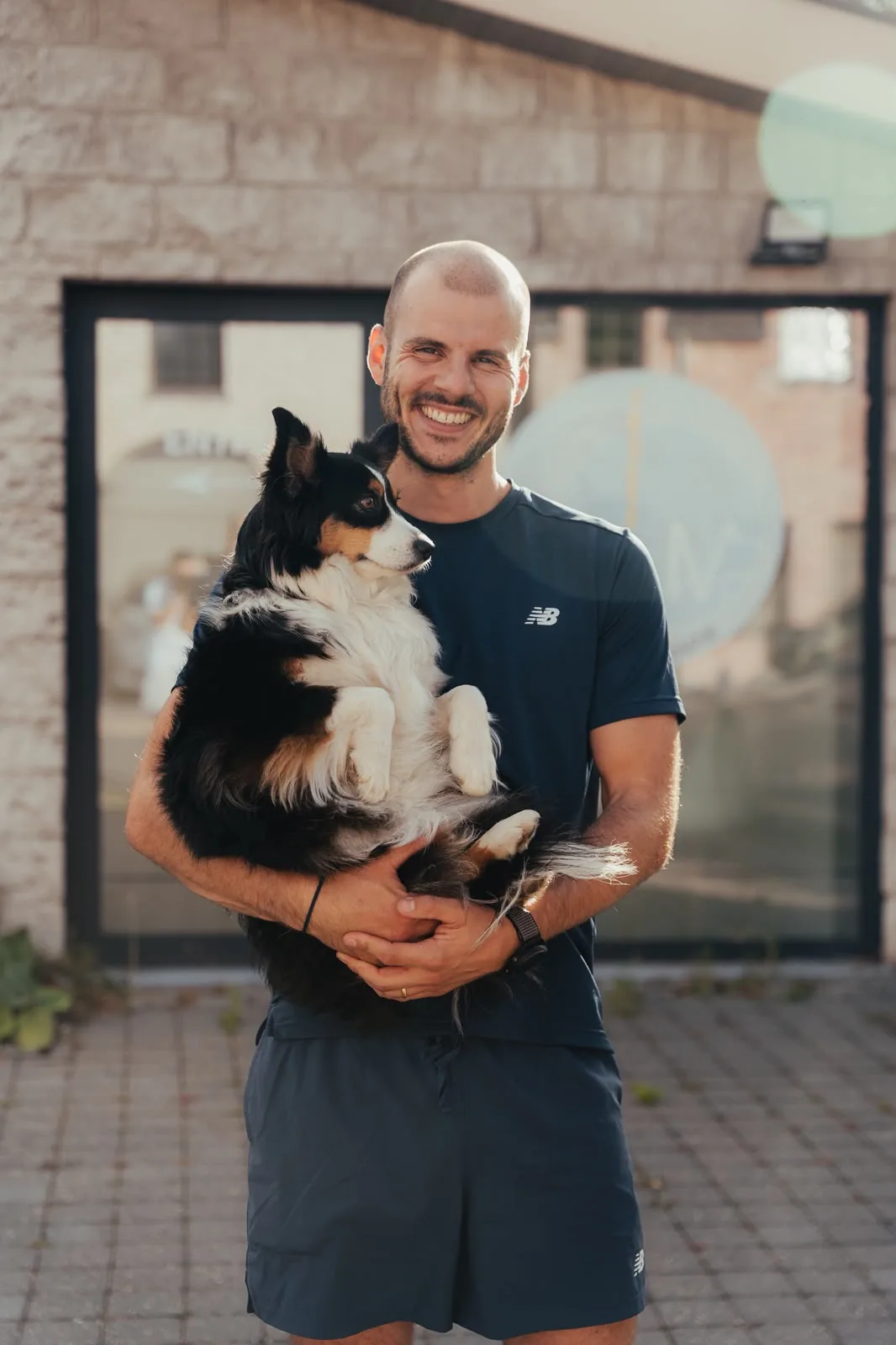 Kinésithérapeute souriant devant l'entrée du centre, un chien dans les bras