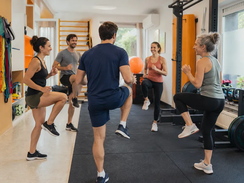 Cinq personnes en tenue de sport qui montent le genou ensemble dans la salle d'entraînement, kinésithérapeute au premier plan
