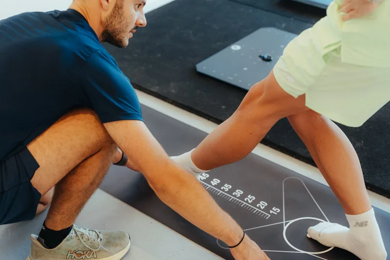 Kinésithérapeute évaluant la mobilité de la jambe d'un sportif sur un tapis de mesure gradué