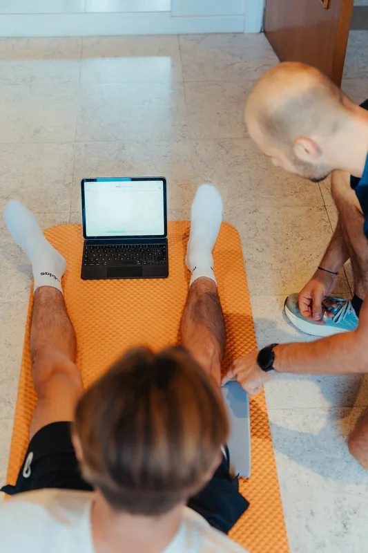 Vue plongeante sur un patient allongé jambes tendues, tablette affichant un graphique de mesure.